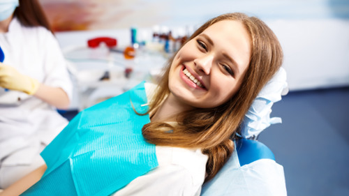 Smiling young woman in dental chair wearing bib during hygiene appointment in Houston dental office
