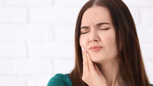 woman in teal shirt in pain holding jaw | tooth extractions tanglewood 